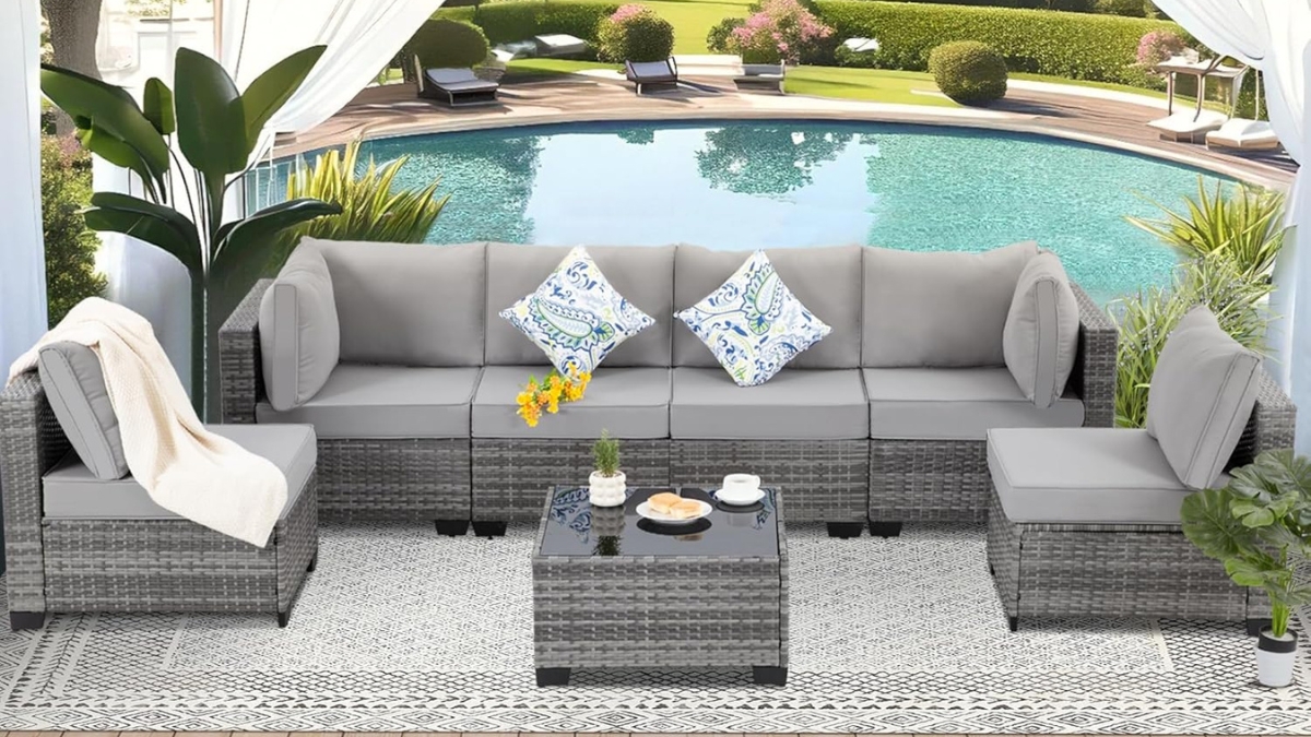 Gray 7 piece outdoor patio furniture set with cushions and wicker frame arranged around a glass coffee table by a pool.