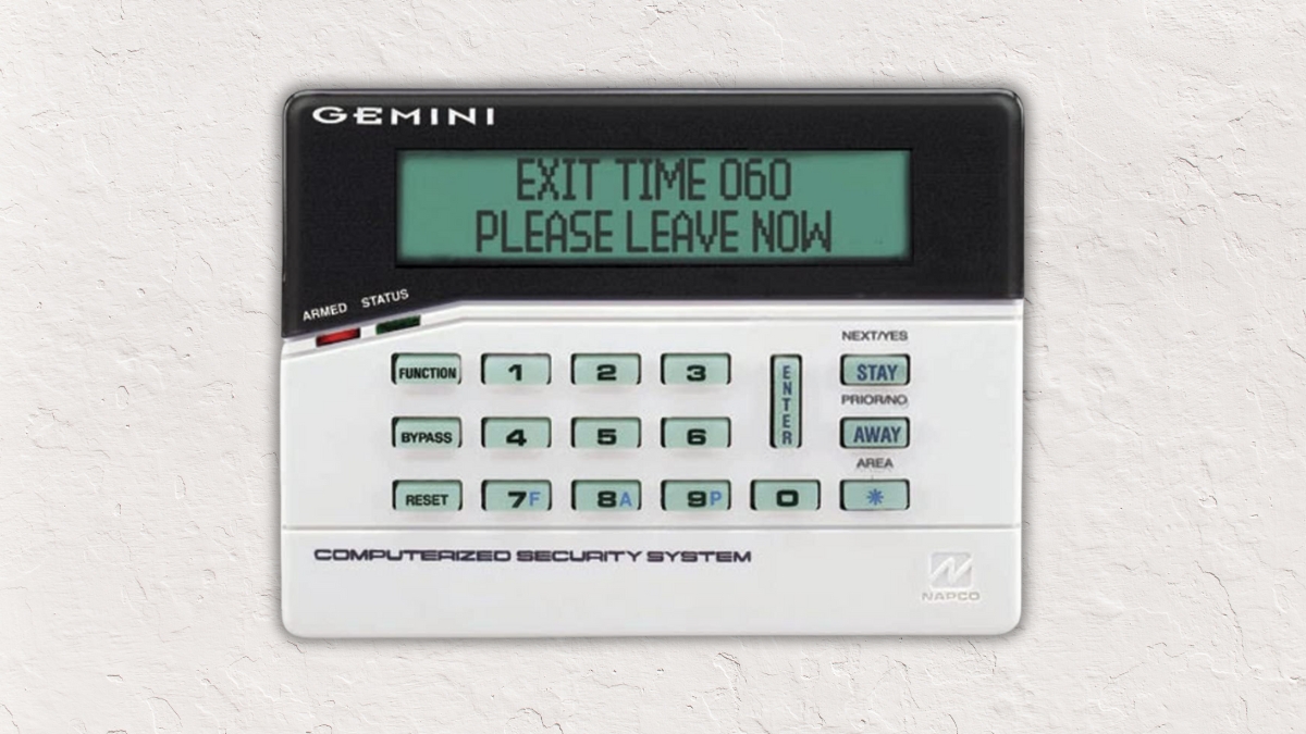 Alphanumeric Napco alarm keypad showing exit countdown and leave message on backlit screen.