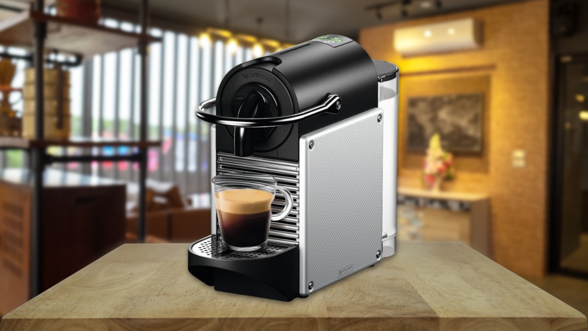 A Nespresso Pixie Espresso Machine sits on a wooden counter with a fresh espresso shot in a clear glass cup.