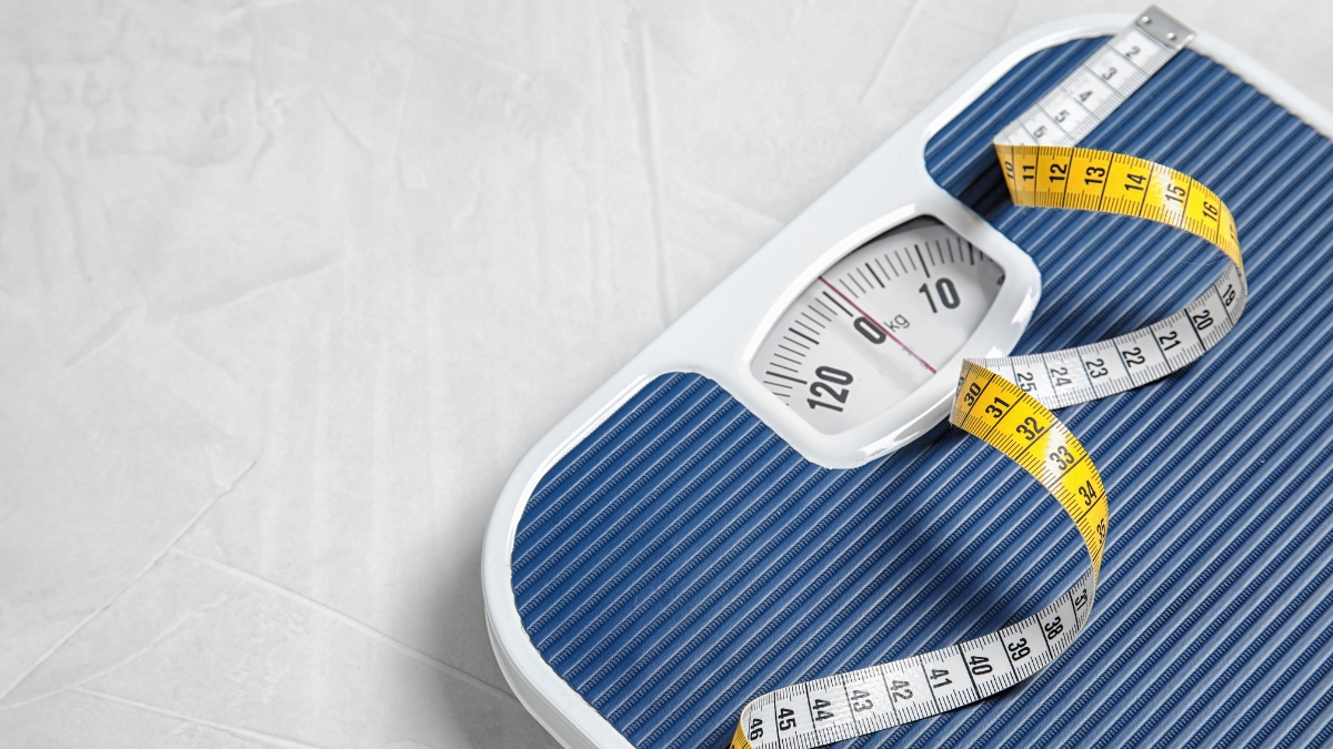 A blue analog bathroom scale with a yellow and white measuring tape placed on top, symbolizing weight tracking and body composition monitoring.