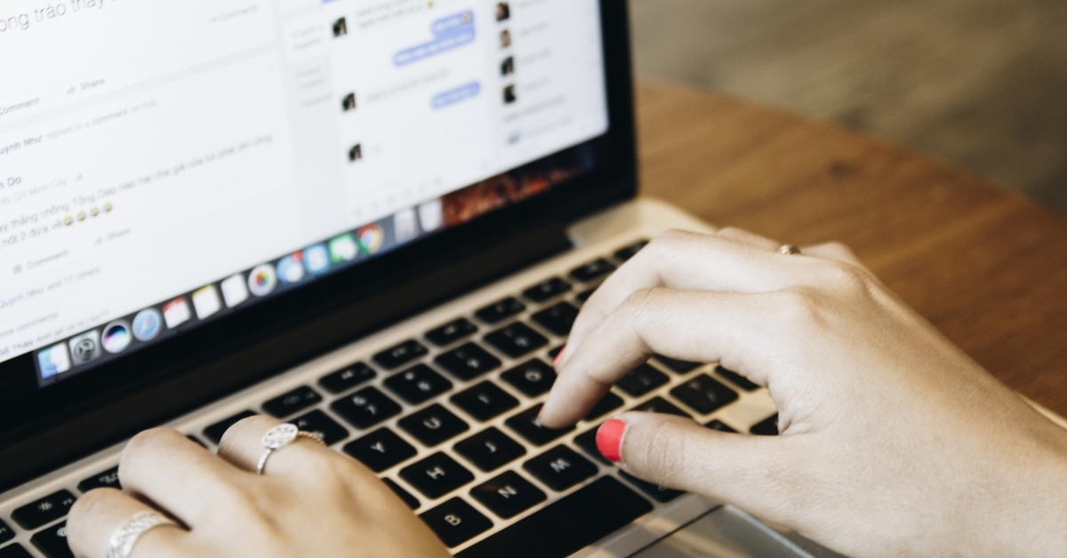 Hands typing on laptop keyboard while messaging online on a social media platform
