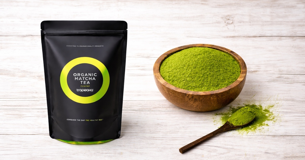 TROPEAKA Organic Matcha Tea powder in black resealable pouch beside bowl of vibrant green Japanese ceremonial matcha on wooden surface