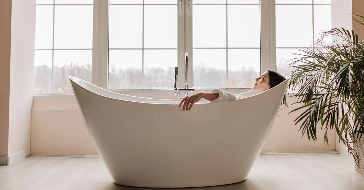 Person relaxing in freestanding bathtub with BADESOFA Bath Pillows near large window