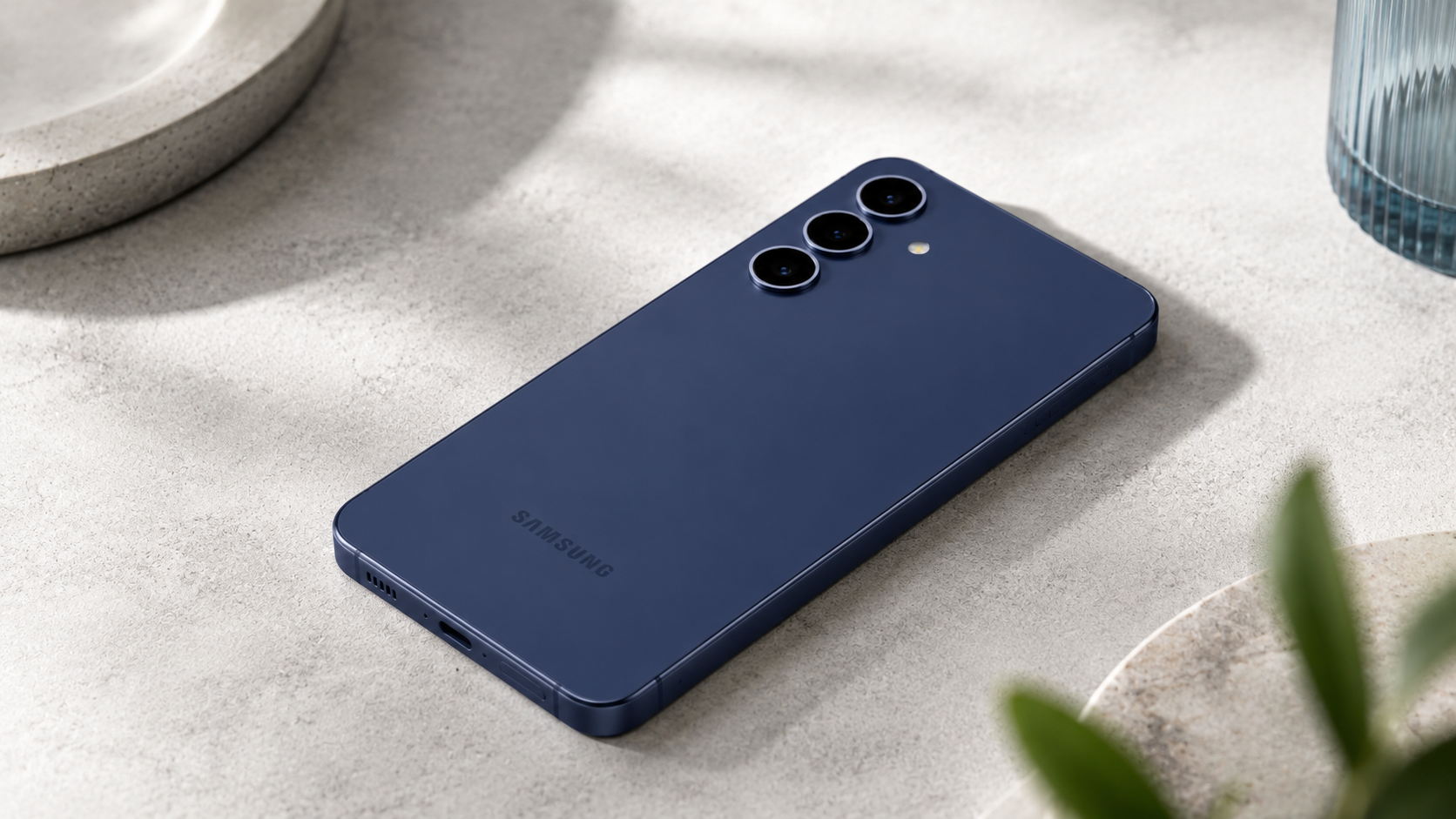Samsung Galaxy S25 FE 5G smartphone in navy blue lying flat on a light stone surface, showcasing its triple rear camera system, slim design, and premium matte finish in a modern lifestyle setting.