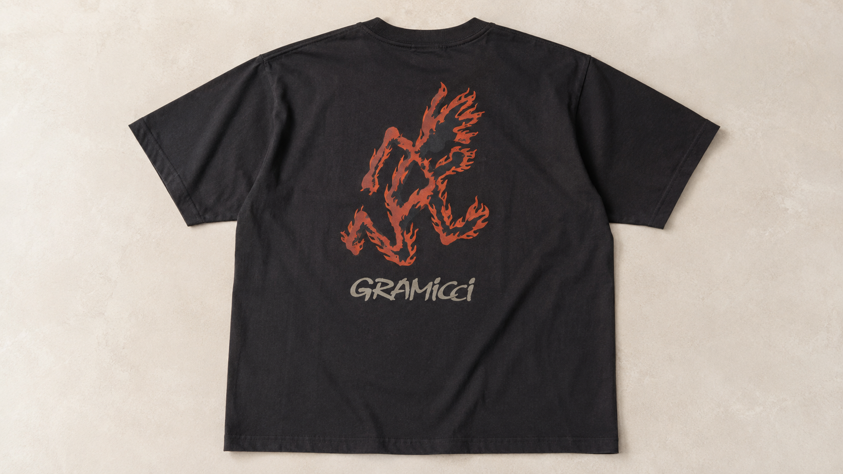 Gramicci Flame Tee in charcoal featuring a large flame-inspired running man graphic and Gramicci logo on the back, laid flat on a neutral background.