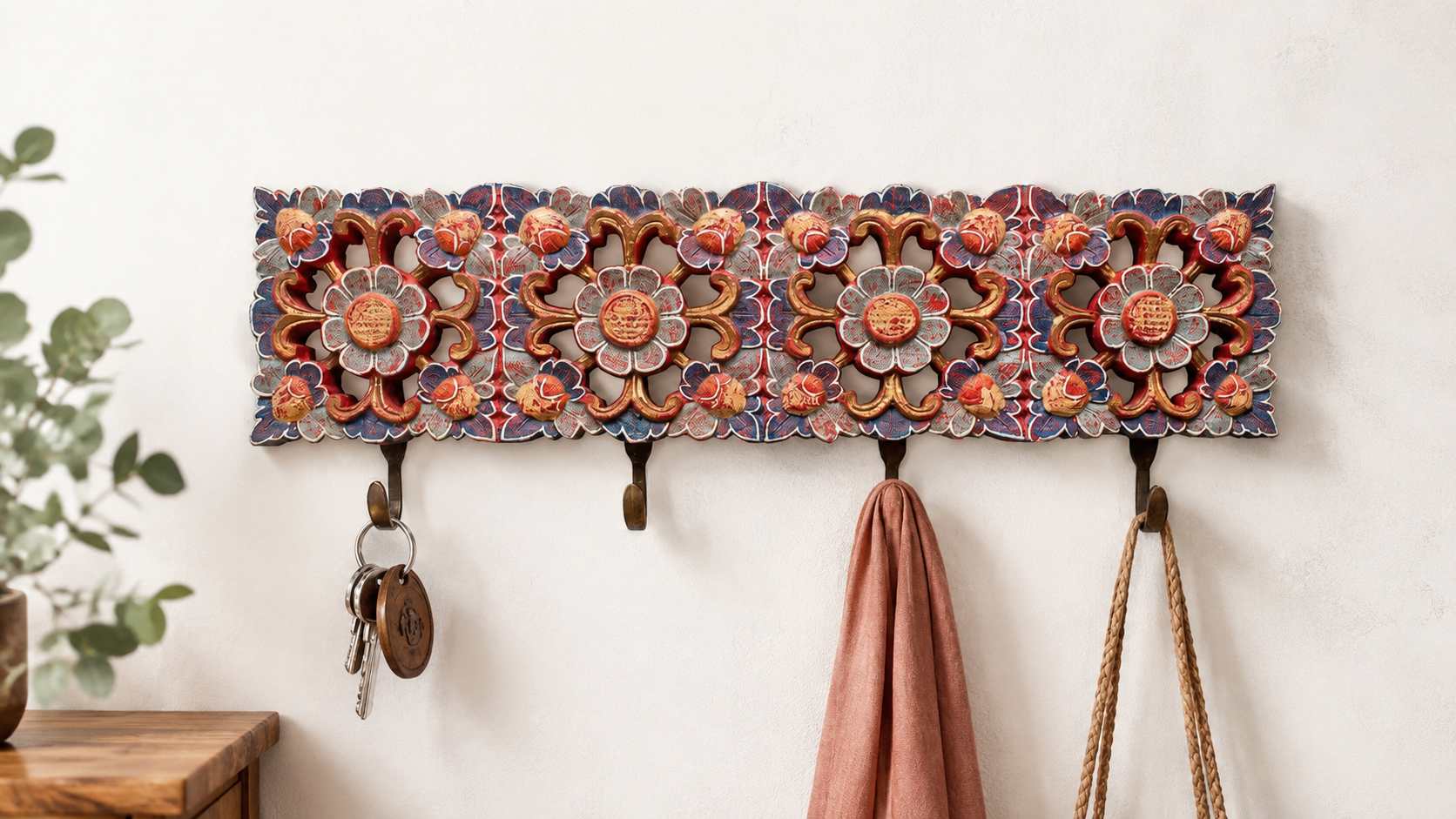 Djiwa carved floral wall hanger with four hooks, displayed on a neutral wall with keys, scarf, and woven bag.