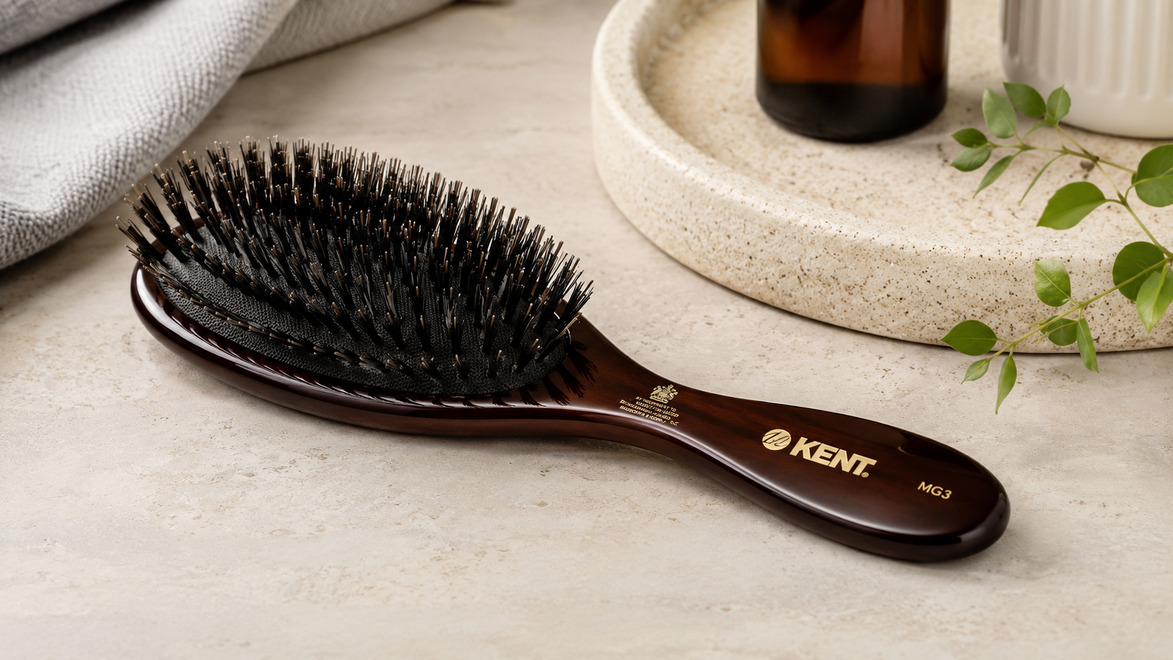 Kent MG3 Men’s Oval Hair Brush with natural bristles and a dark wood handle displayed on a stone countertop in a modern bathroom setting.