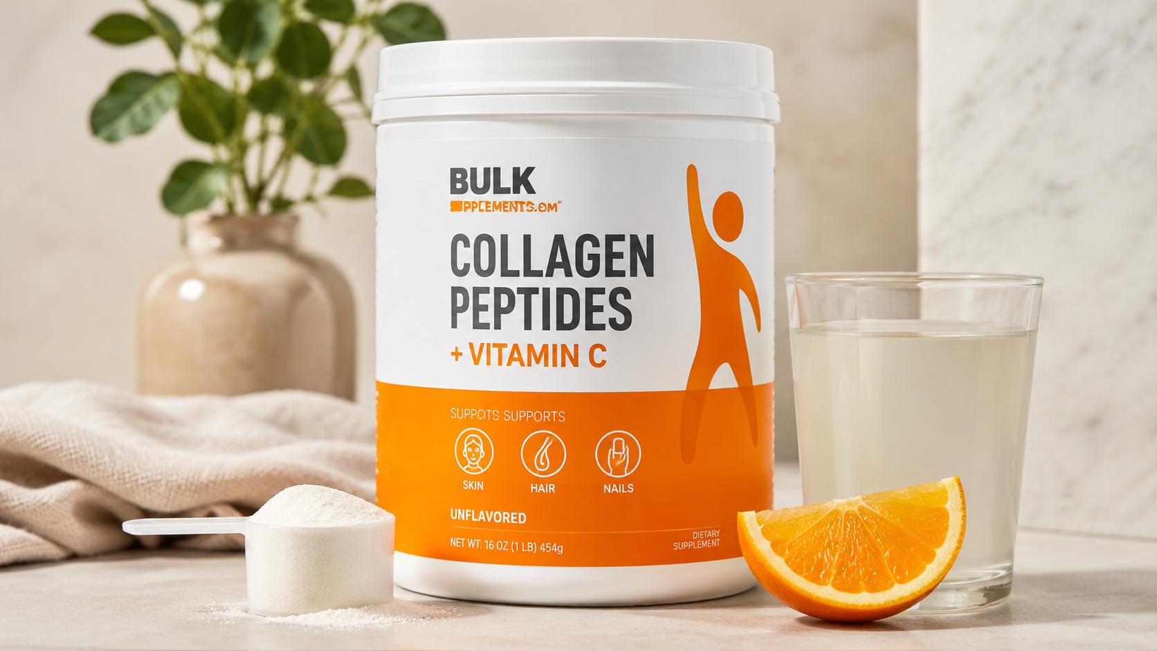 Bulk Supplements Collagen Peptides + Vitamin C powder in a white container with a scoop of collagen powder, glass of mixed supplement, and fresh orange slice on a clean countertop.