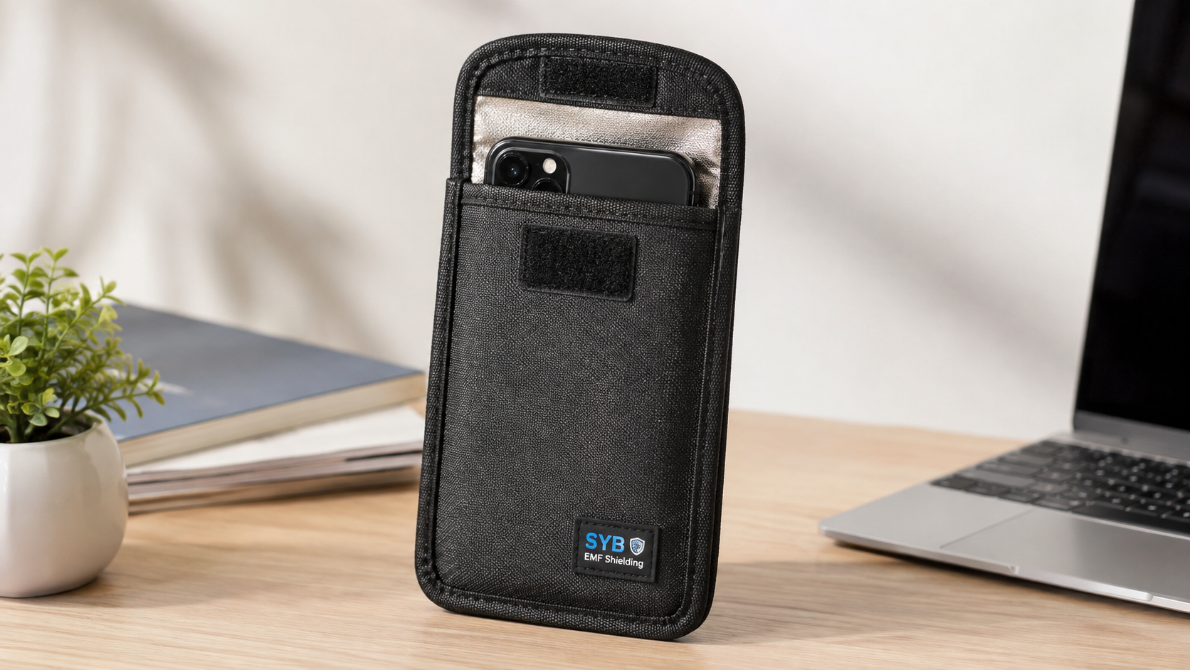 SYB Phone Pouch EMF radiation shielding pouch with a smartphone partially inserted, displayed on a modern office desk with a laptop and plant, showcasing RF and EMF protection for mobile devices.