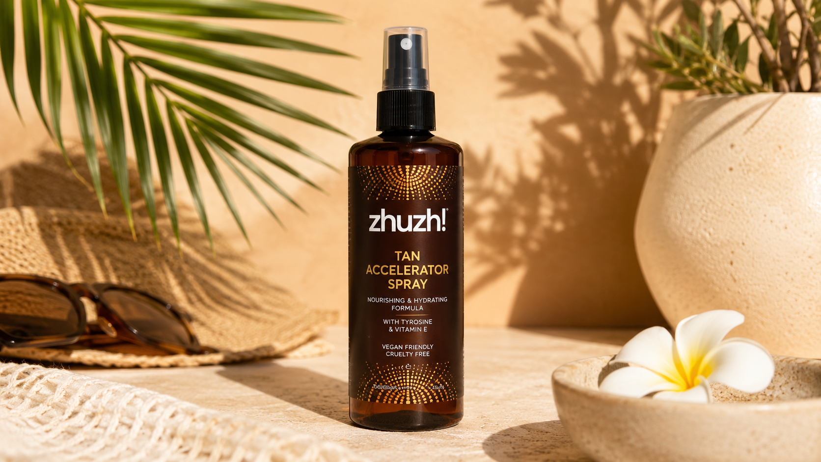 Zhuzh! Tan Accelerator Spray bottle with tyrosine and vitamin E displayed in a tropical beach-inspired setting, ideal for accelerating a natural sun tan while nourishing and hydrating the skin.